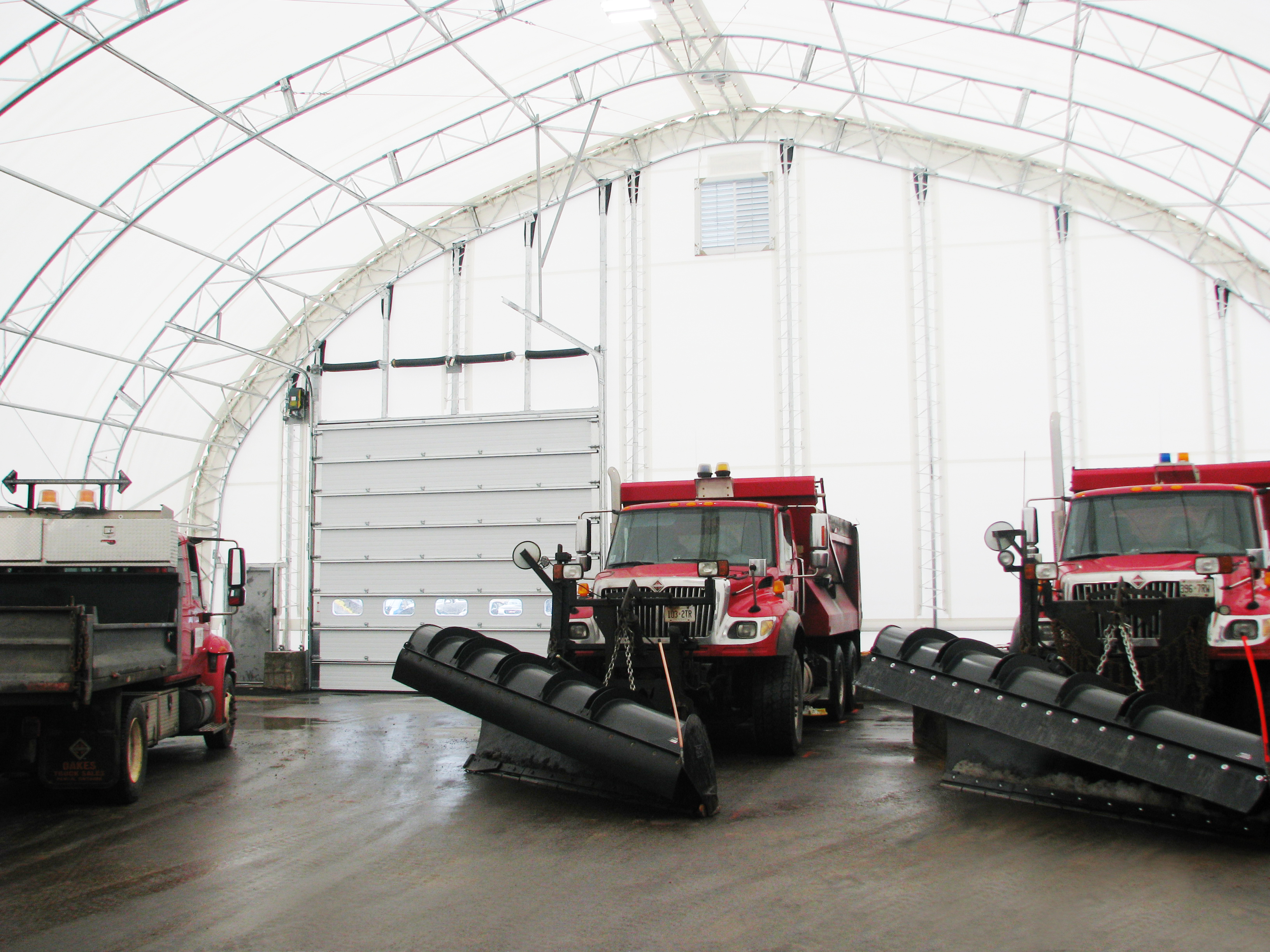 Municipal snowplow trucks inside a fabric building fleet shelter