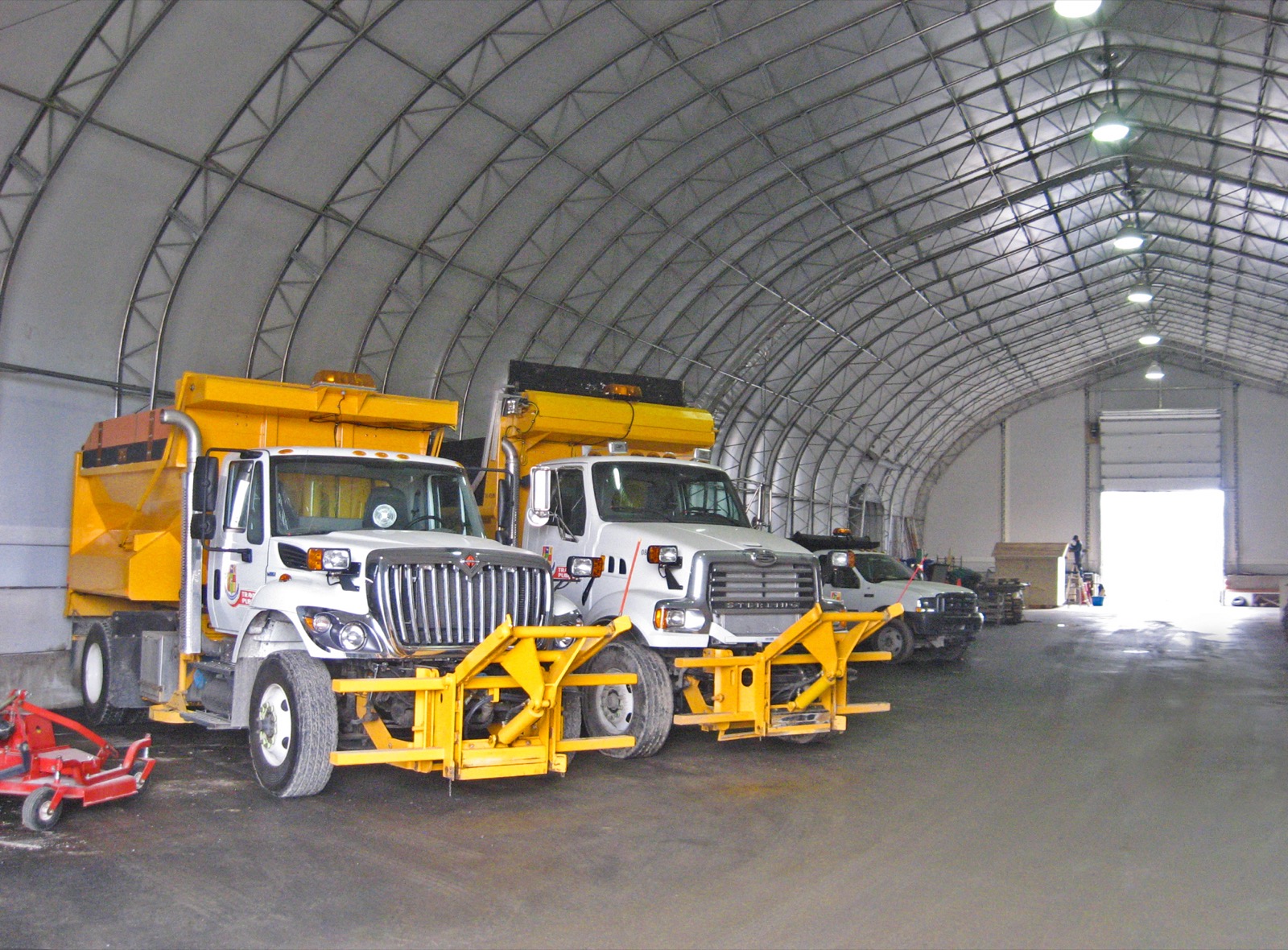 Municipal snowplow trucks stored inside a fabric building fleet garage